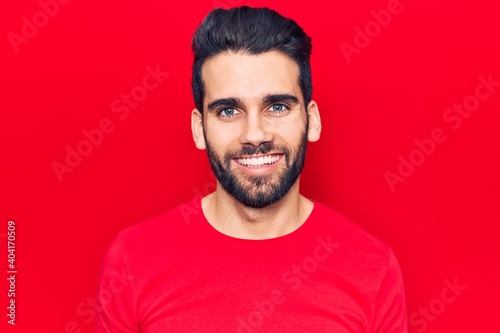 Young handsome man with beard wearing casual t-shirt looking positive and happy standing and smiling with a confident smile showing teeth