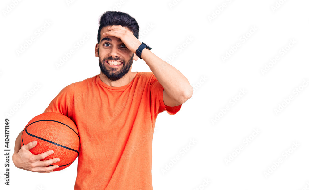 Fototapeta premium Young handsome man with beard hoilding basketball ball stressed and frustrated with hand on head, surprised and angry face