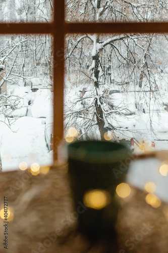 Branches covered with snow. The view from the window on a snowy morning. Warm lights in the defocus in the foreground.