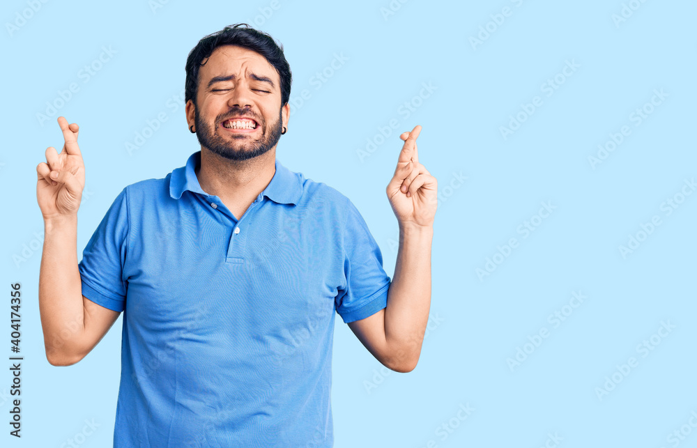 Fototapeta premium Young hispanic man wearing casual clothes gesturing finger crossed smiling with hope and eyes closed. luck and superstitious concept.