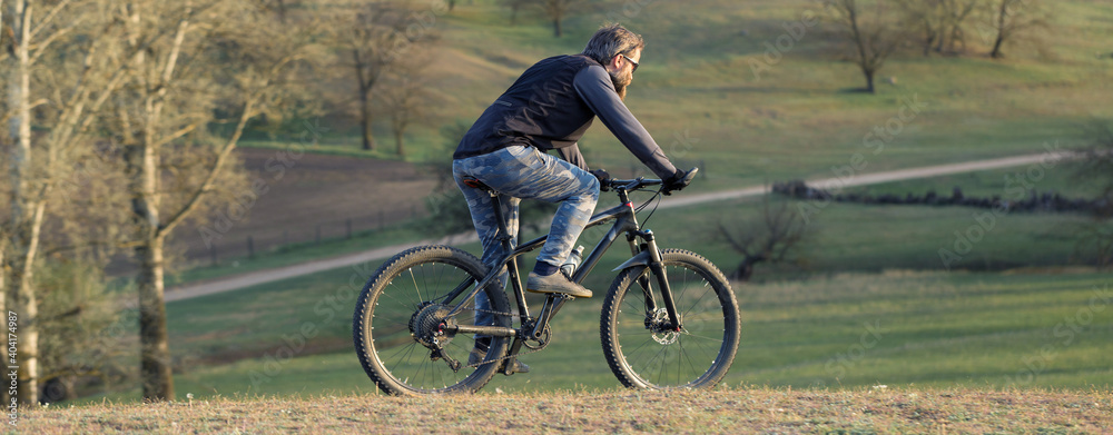 Fototapeta premium Sports brutal bearded guy on a modern mountain bike. Cyclist on the green hills in the spring.