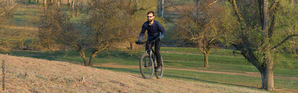 Fototapeta premium Cyclist in shorts and jersey on a modern carbon hardtail bike with an air suspension fork standing on a cliff against the background of fresh green spring forest