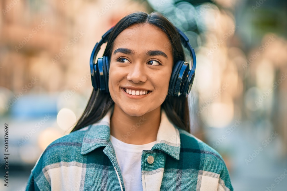 Young latin girl smiling happy using headphones at the city. Young latin girl smiling happy using headphones at the city.