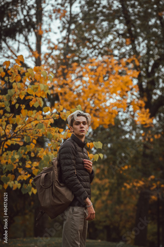 Male with bleached hair wearing fall colors while surrounded by very orange trees from autumn