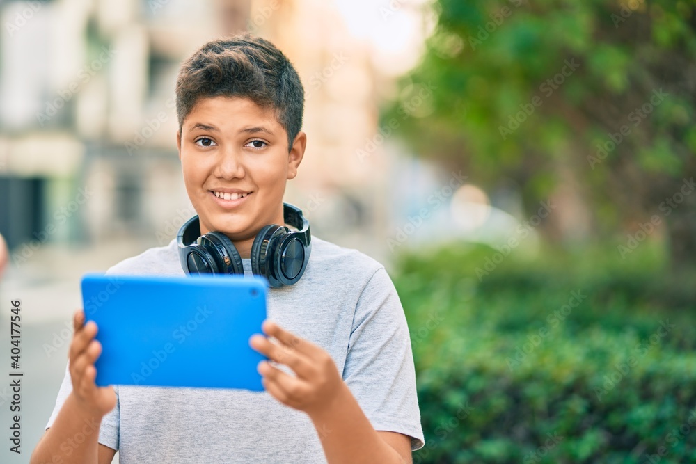 Adorable latin boy smiling happy using headphones and touchpad at the park. Adorable latin boy smiling happy using headphones and touchpad at the park.
