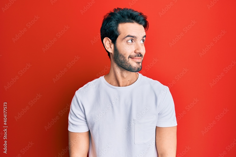 Fototapeta premium Young hispanic man wearing casual white tshirt smiling looking to the side and staring away thinking.