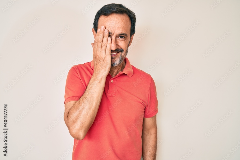 Middle age hispanic man wearing casual clothes covering one eye with hand, confident smile on face and surprise emotion. Middle age hispanic man wearing casual clothes covering one eye with hand, confident smile on face and surprise emotion.