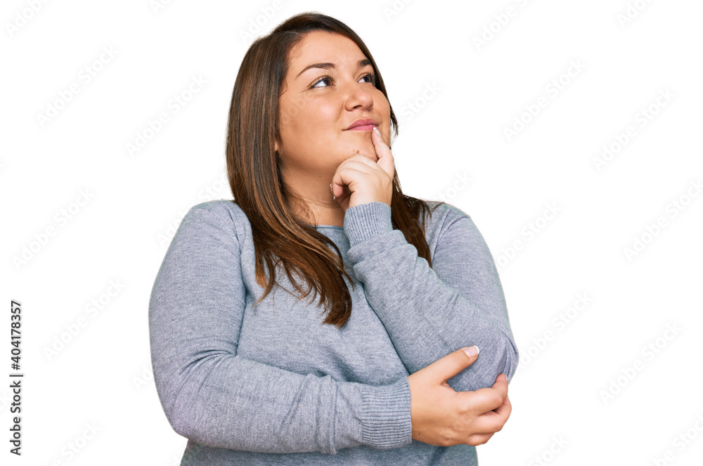Beautiful brunette plus size woman wearing casual clothes with hand on chin thinking about question, pensive expression. smiling with thoughtful face. doubt concept. Beautiful brunette plus size woman wearing casual clothes with hand on chin thinking about question, pensive expression. smiling with thoughtful face. doubt concept.