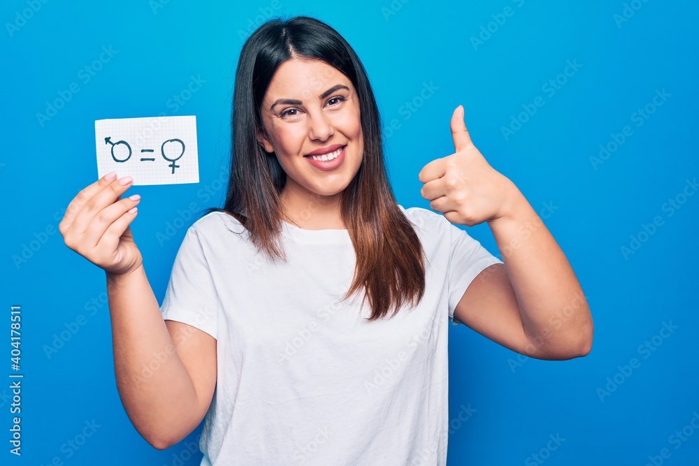 Beautiful woman asking for sex discrimination holding paper with gender equality concept smiling happy and positive, thumb up doing excellent and approval sign Beautiful woman asking for sex discrimination holding paper with gender equality concept smiling happy and positive, thumb up doing excellent and approval sign