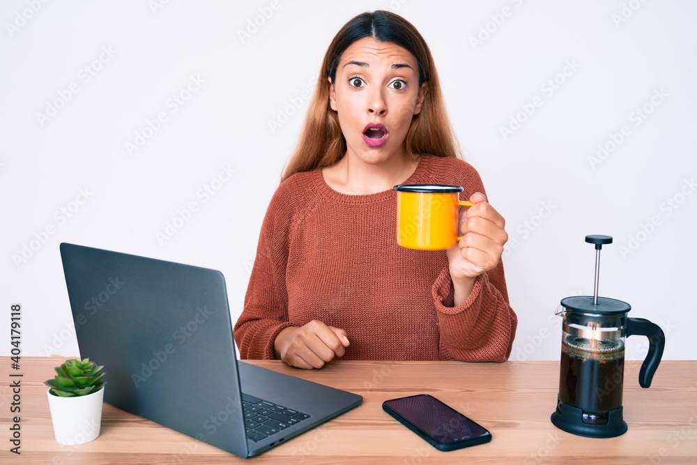 Young brunette woman working at the office drinking a cup of coffee scared and amazed with open mouth for surprise, disbelief face Young brunette woman working at the office drinking a cup of coffee scared and amazed with open mouth for surprise, disbelief face