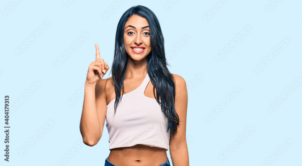 Beautiful hispanic woman wearing casual clothes showing and pointing up with finger number one while smiling confident and happy. Beautiful hispanic woman wearing casual clothes showing and pointing up with finger number one while smiling confident and happy.