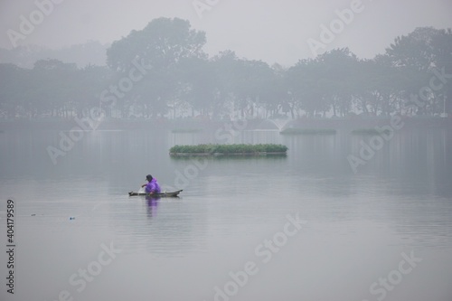 Lone fisherman in a boat on a lake on a misty gray day in rural Vietnam