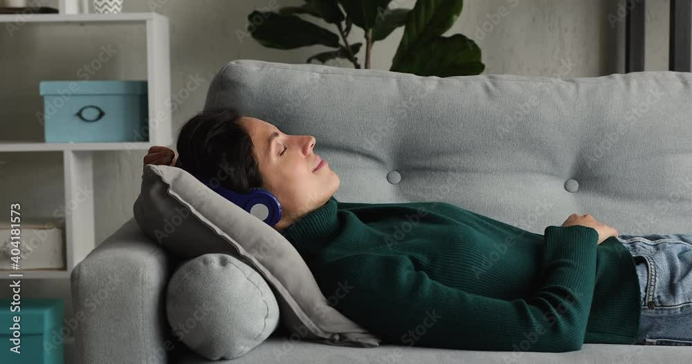 Tranquil woman lying on sofa cushion with eyes closed listen music through wireless headphones feels peaceful falling asleep. No stress, relaxation at home, quiet mind hearing audio meditation concept Tranquil woman lying on sofa cushion with eyes closed listen music through wireless headphones feels peaceful falling asleep. No stress, relaxation at home, quiet mind hearing audio meditation concept