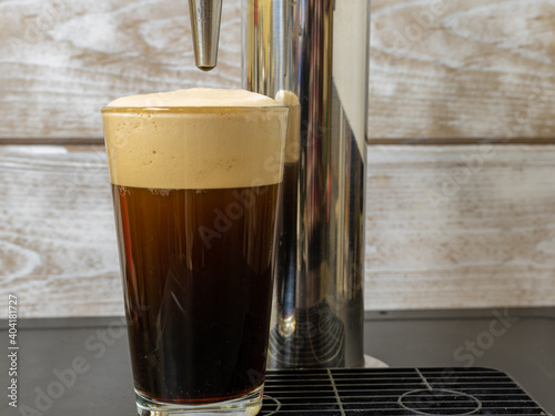 Photography Nitro Cold Brew coffee in a clear glass with fine nitrogen bubbles and a smooth texture on a keg coffee dispenser
