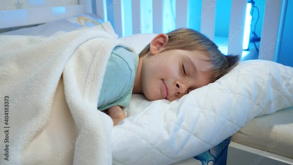 Portrait of cute toddler boy lying in bed and sleeping at night. Calm beautiful child in bed