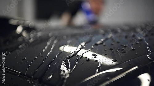 Slow motion closeup blowing off water from freshly washed black car with air. Car wash and detailing service.