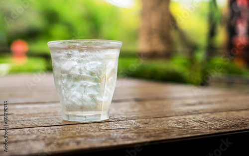 Ice in a glass of water on a wood table, the background is blurred green.