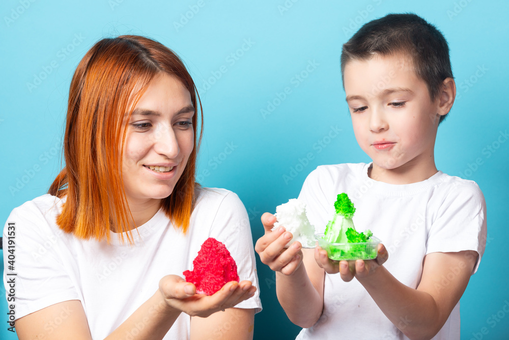 Mom and son are holding grown red and green crystals, which they made on their own as a result of a chemical experiment on a blue background. A chemical experiment in growing crystals