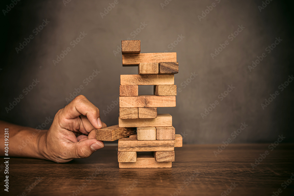 Close-up hand pull wooden block from other the wood block stacked in tower shape concepts of financial risk management and strategic planning. Close-up hand pull wooden block from other the wood block stacked in tower shape concepts of financial risk management and strategic planning.