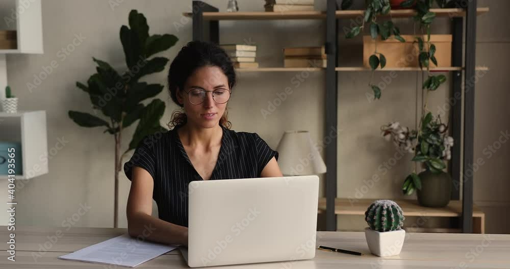 Focused woman employee wear glasses working on laptop in office room. Concentrated business woman corresponding with corporate client, check e-mail. Busy workday at workplace using modern tech concept