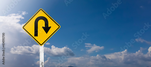 U-turn sign on white pole with clouds and blue sky background.