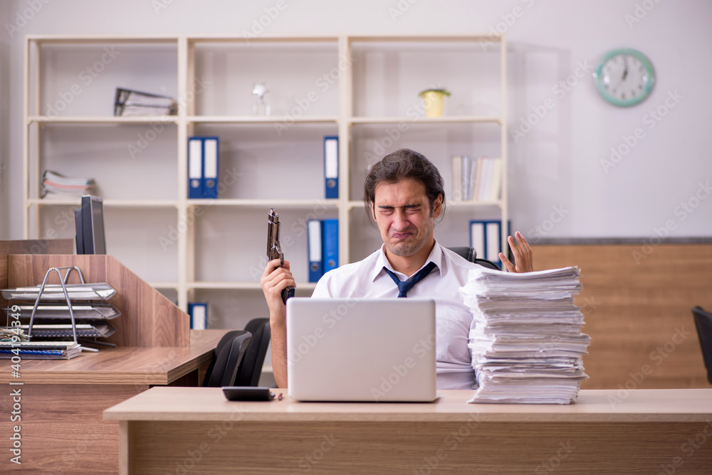 Young male employee unhappy with excessive work in the office Young male employee unhappy with excessive work in the office