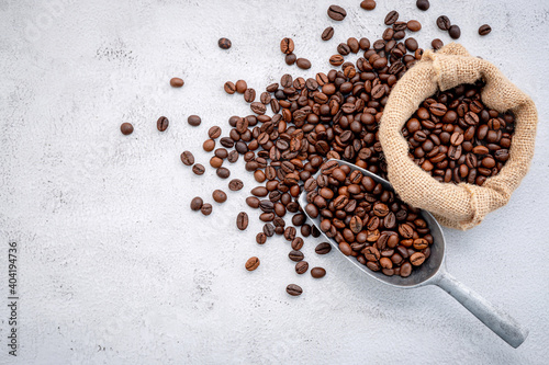 Roasted coffee beans with scoops setup on white concrete background.