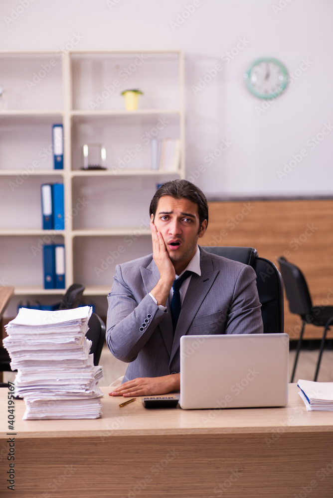 Young male employee unhappy with excessive work in the office Young male employee unhappy with excessive work in the office