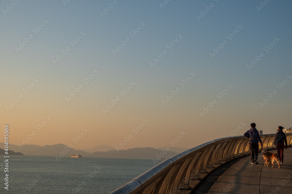 Obraz premium A couple walk their dog along the embankment of Hong Kong Island at the sunset 