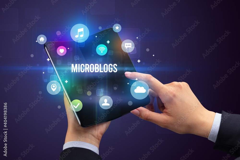 Businessman holding a foldable smartphone with MICROBLOGS inscription, social media concept Businessman holding a foldable smartphone with MICROBLOGS inscription, social media concept