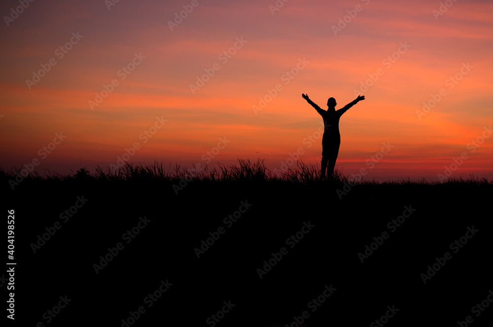 Silhouette of young traveler standing alone and open arms watched beautiful view sunset on top of the mountain. She is happy and success to be with herself and stay with nature at twilight time.