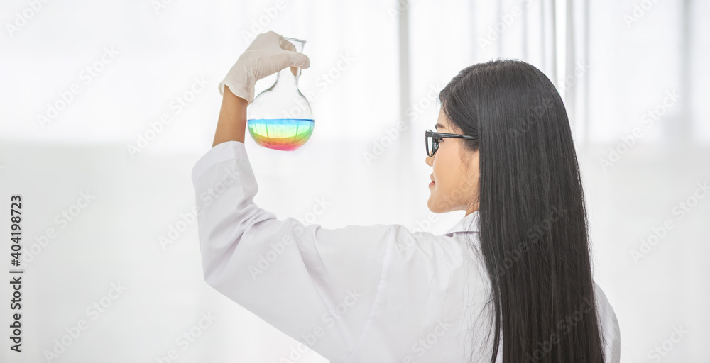 Naklejka premium Young Asian scientist woman holding and looking at the chemical flasks in the laboratory 