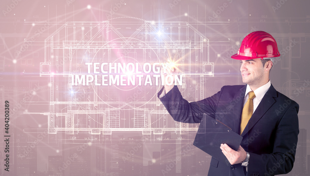 Handsome architect with helmet drawing TECHNOLOGY IMPLEMENTATION inscription, new technology concept Handsome architect with helmet drawing TECHNOLOGY IMPLEMENTATION inscription, new technology concept