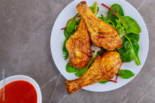 Roasted spicy chicken drumstick with salad and sauce on gray background.