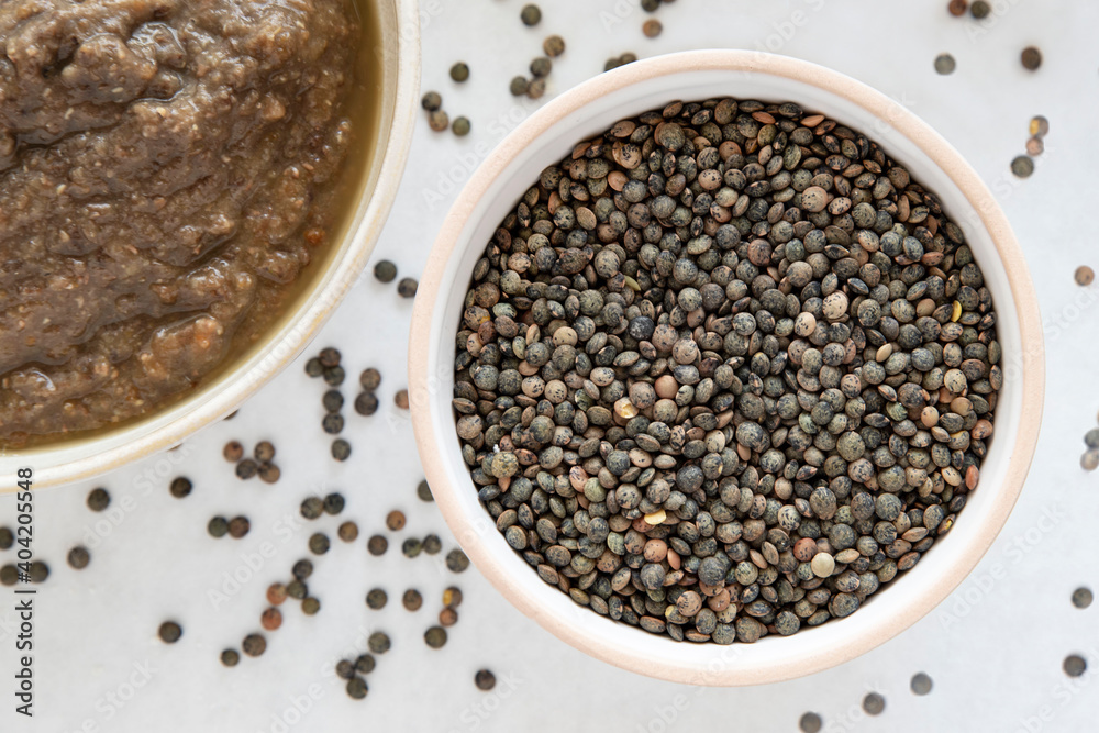 Close-up of a bowl of raw lentils with a partial view of a lentil soup dish Close-up of a bowl of raw lentils with a partial view of a lentil soup dish