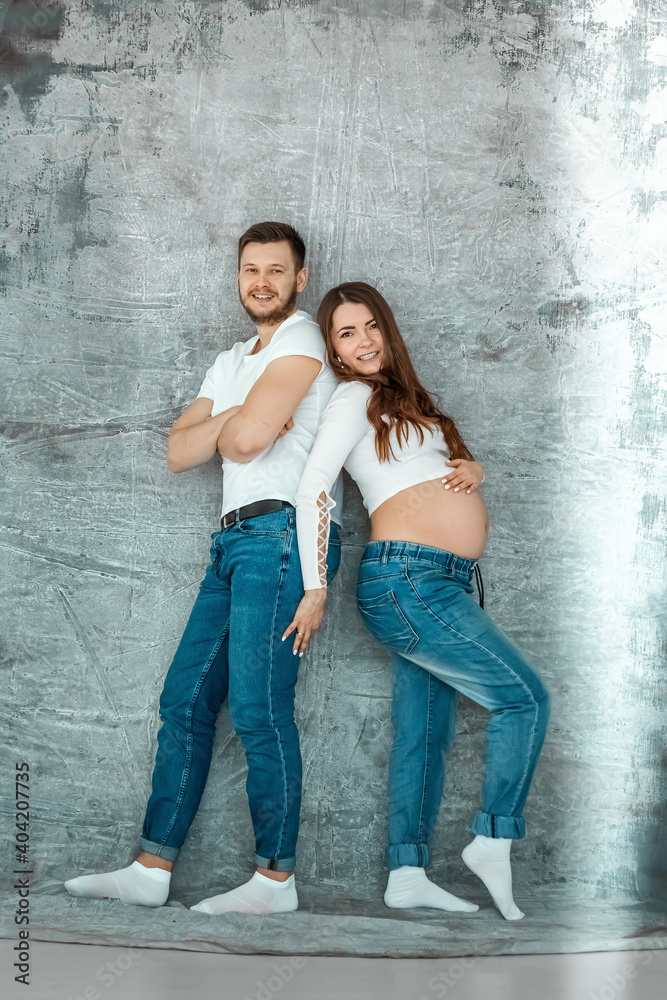 A pregnant girl and her husband are standing against the wall. Beautiful belly of a young attractive pregnant girl. Family, marriage, childbirth concept.
