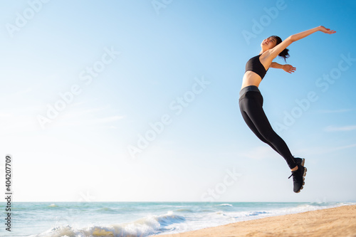 Young Asian healthy athletic slim woman smiling jumping on beach