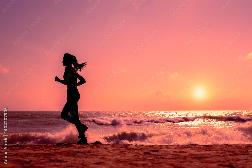 Silhouette slim sport female running on beach in sunset or sunrise