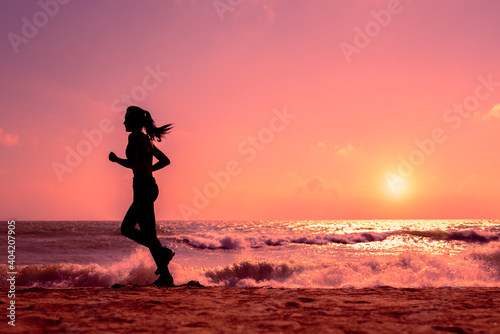 Silhouette slim sport female running on beach in sunset or sunrise
