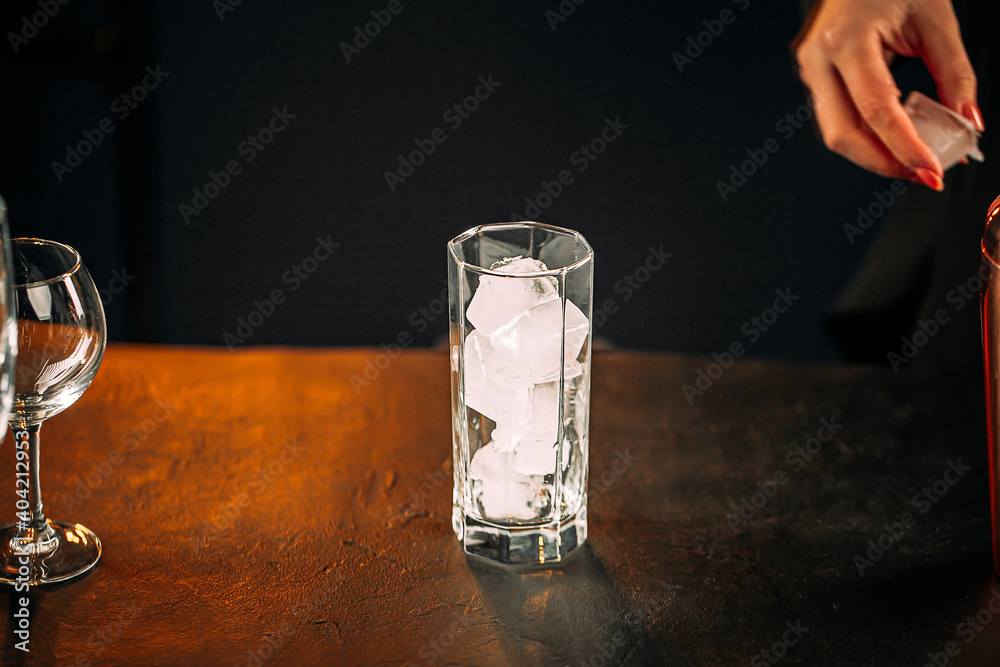 Glass full of ice ready to be mixed in a cocktail with a woman's hand