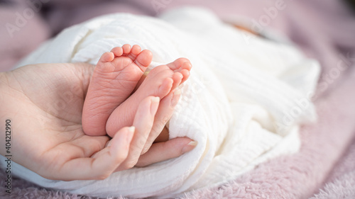 close up asian woman mother hand holding small baby infant feet while sleeping on soft bed covered with white cloth.