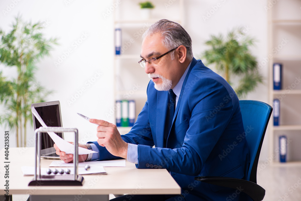 Old male employee businessman and meditation balls on the desk