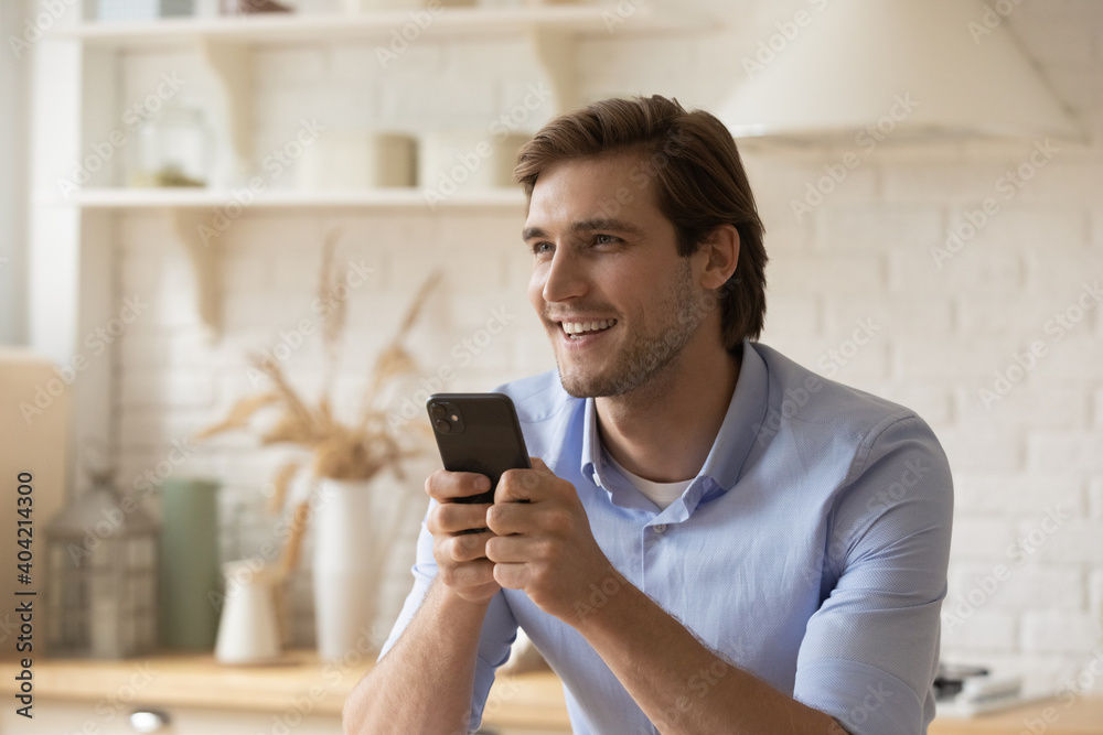 Happy millennial Caucasian man sit at home use modern smartphone look aside talking chatting. Smiling young male have fun browsing wireless internet on cellphone. Online communication concept. Happy millennial Caucasian man sit at home use modern smartphone look aside talking chatting. Smiling young male have fun browsing wireless internet on cellphone. Online communication concept.