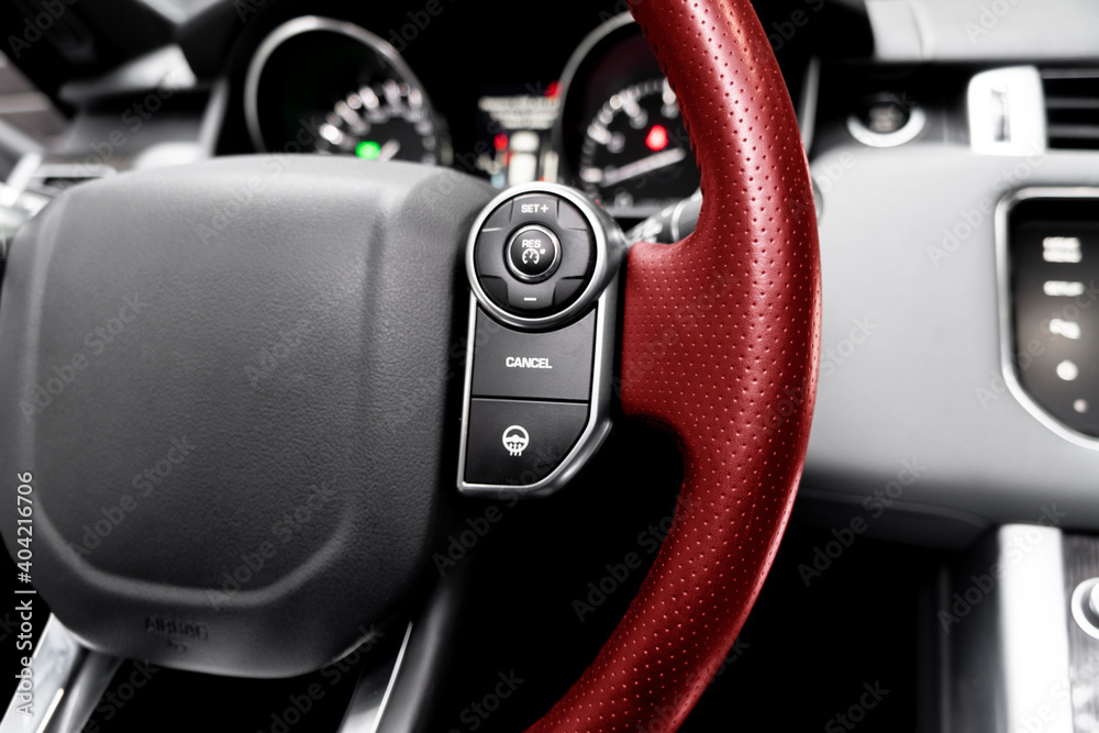 Cruise control buttons on the red perforated leather steering wheel of a modern car.  Car interior details