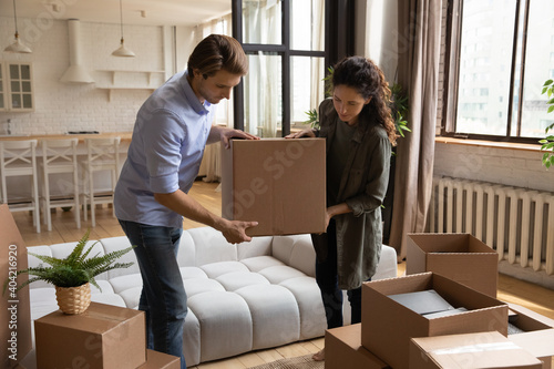 Millennial Caucasian man and woman pack cardboard boxes relocate to own dwelling or apartment together. Young couple renters move to new home or house. Delivery service, real estate, rental concept.