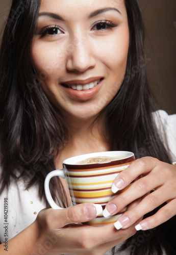 Young asian woman holding a coffee cup over brown background, close up picture