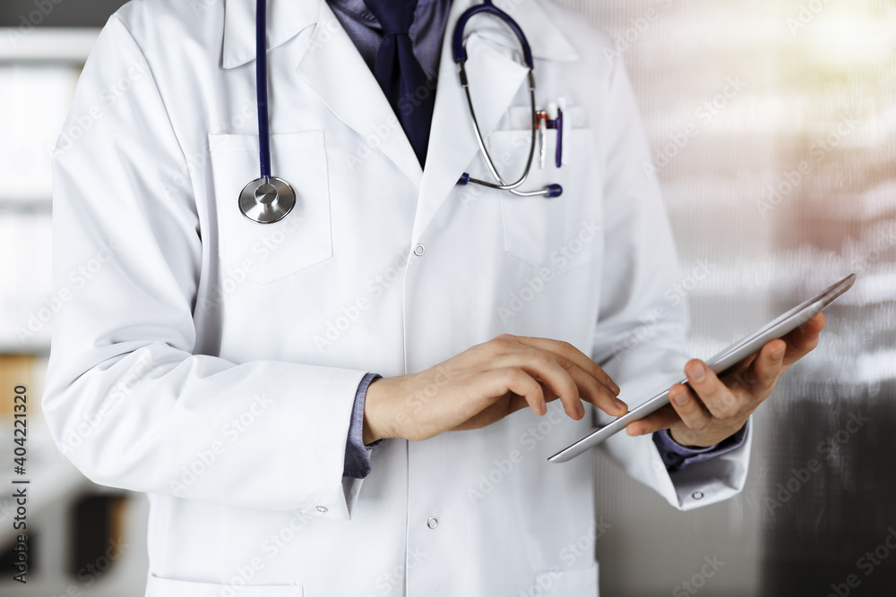 Unknown male doctor using tablet computer in sunny clinic, closeup. Perfect medical service in hospital. Medicine and healthcare concept Unknown male doctor using tablet computer in sunny clinic, closeup. Perfect medical service in hospital. Medicine and healthcare concept