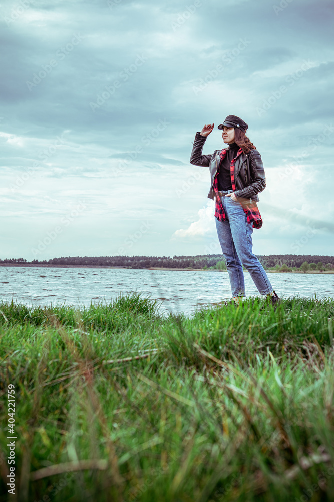 beautiful woman in jeans pants and leather coat and cap posing at lake beach beautiful woman in jeans pants and leather coat and cap posing at lake beach
