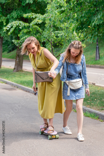 family on a walk in the park. daughter teaches mom to skateboard. Outdoor lifestyle picture on a sunny summer day. © Елена Гурова