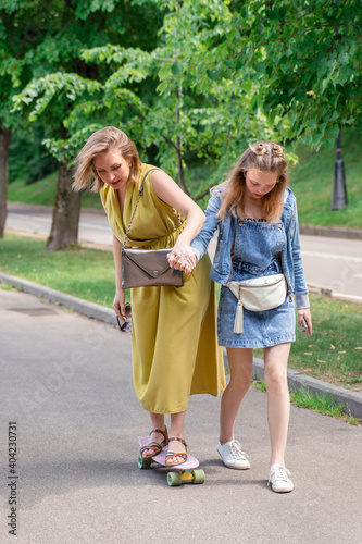 family on a walk in the park. daughter teaches mom to skateboard. Outdoor lifestyle picture on a sunny summer day.